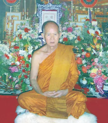 Phra Thep Mongkhon Yan (Luang Pho Son Analayo) seated before a shrine decked with flowers